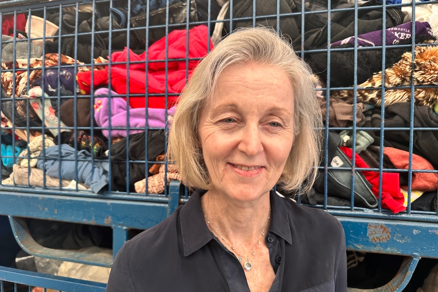 Older woman smiles as she stands in front of piles of donated clothes