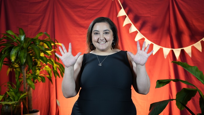 Person in front of a red backdrop with plants and triangular banners.