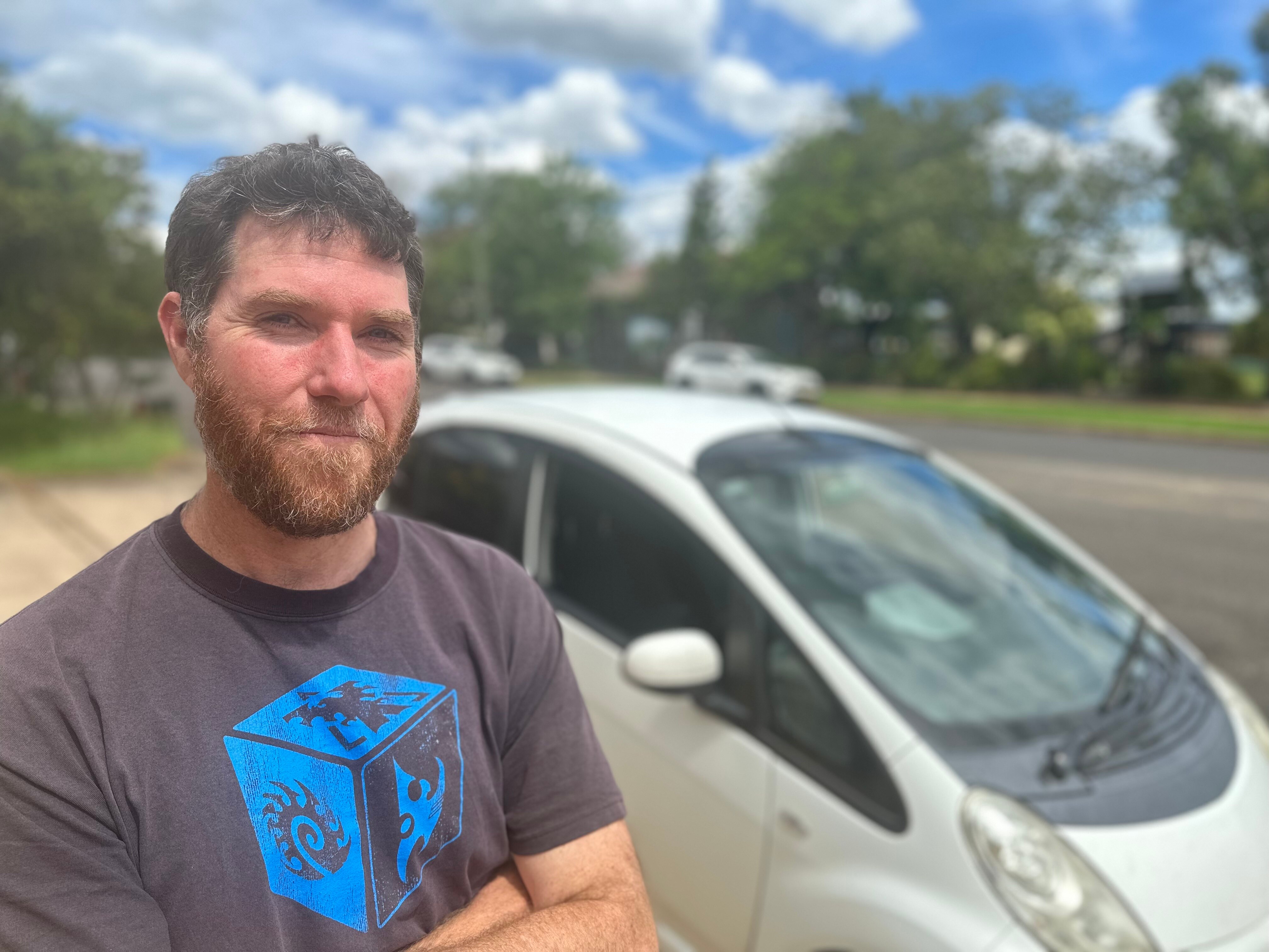 A man stands outside in front of his white sedan.