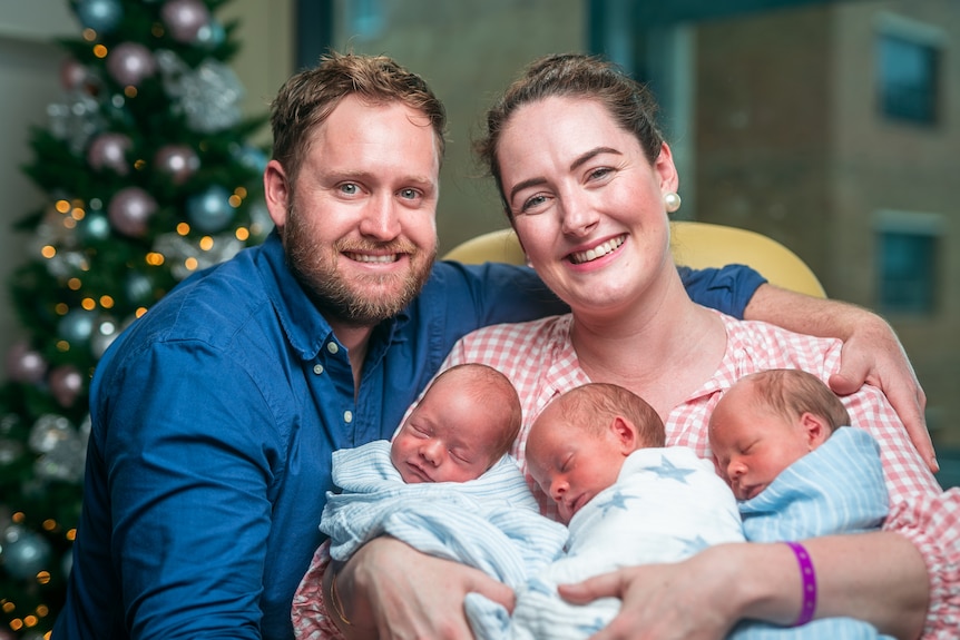 Dr Josephine Nunn and Cohen Nunn with their triplets Maverick, Louis and Winston, with a Christmas tree behind them.