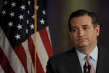 Senator Ted Cruz looks resigned as he stands at a lectern in front of an American flag.