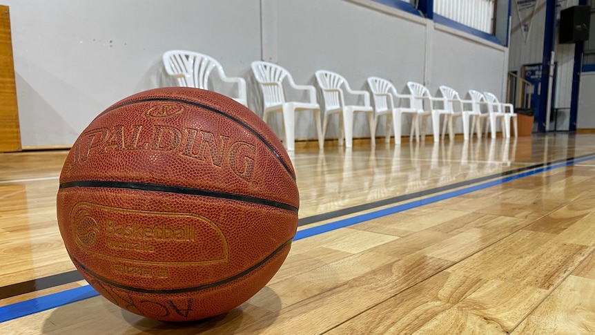 A basketball on an indoor basketball court placed in front of a row of empty bench chairs. 
