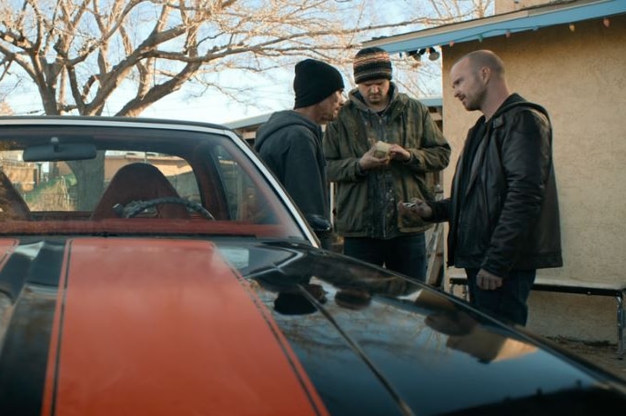 Two men hand money over to a third man while standing next to a car