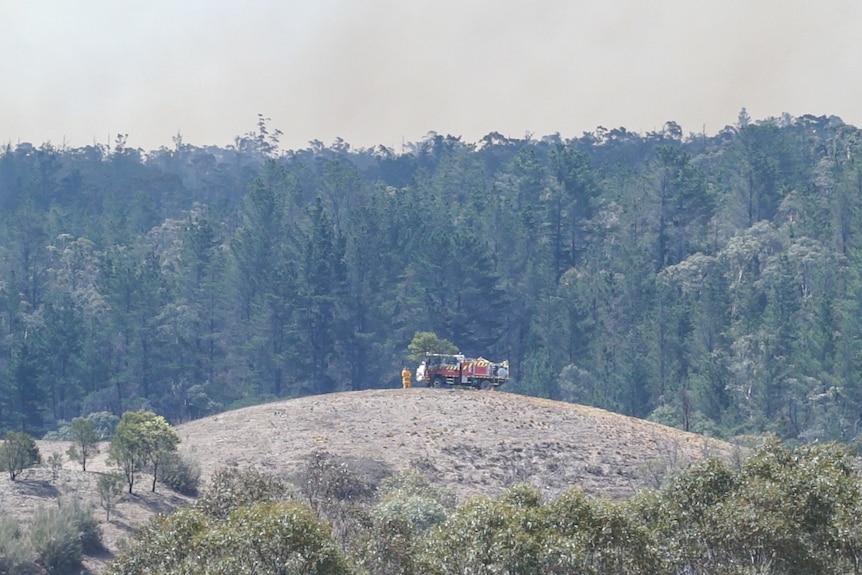 An RFS fire truck sits on top of a hill in front of a forest likely to burn in the bush fires.