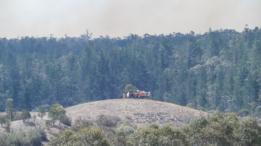 An RFS fire truck sits on top of a hill in front of a forest likely to burn in the bush fires.