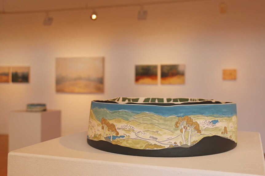 A ceramic artwork depicting Canberra's landscape sitting on a pedestal in the middle of an art exhibition