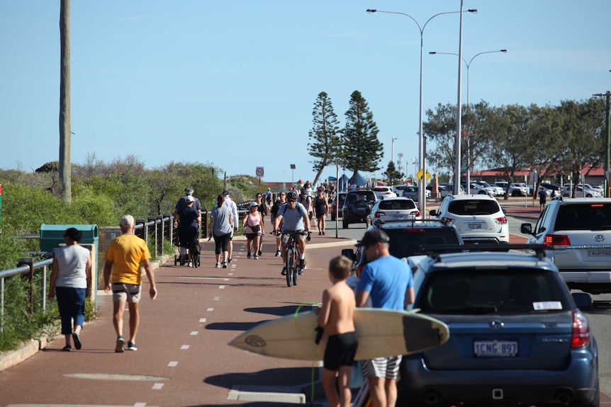 People walk and cycle on beach pathway by a road.