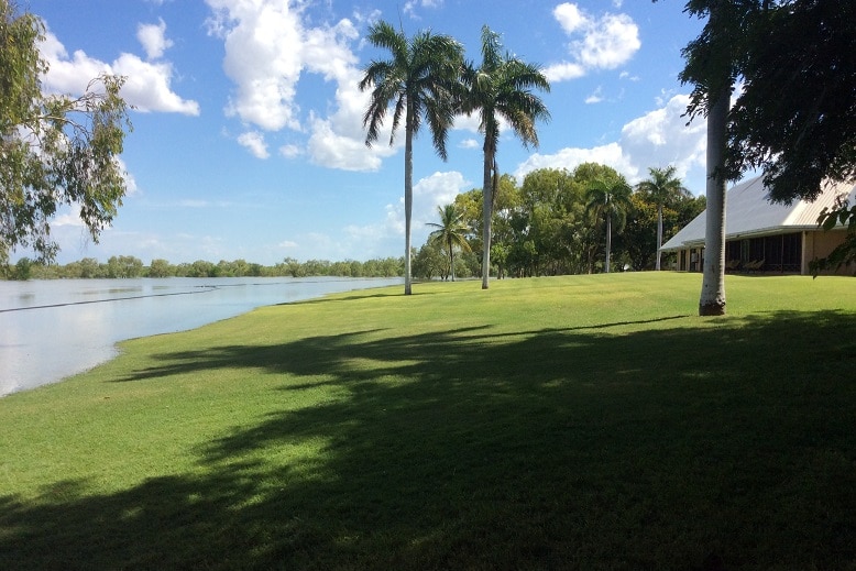 Floodwater to the left of green lawn and a homestead property on the right.