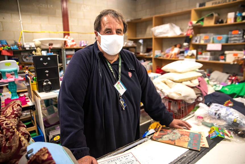 A man wearing a mask stands at a sorting table in an op shop