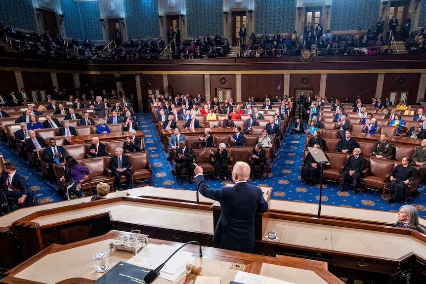 Joe Biden at a lectern surrounded by people in the US House of Representatives chamber