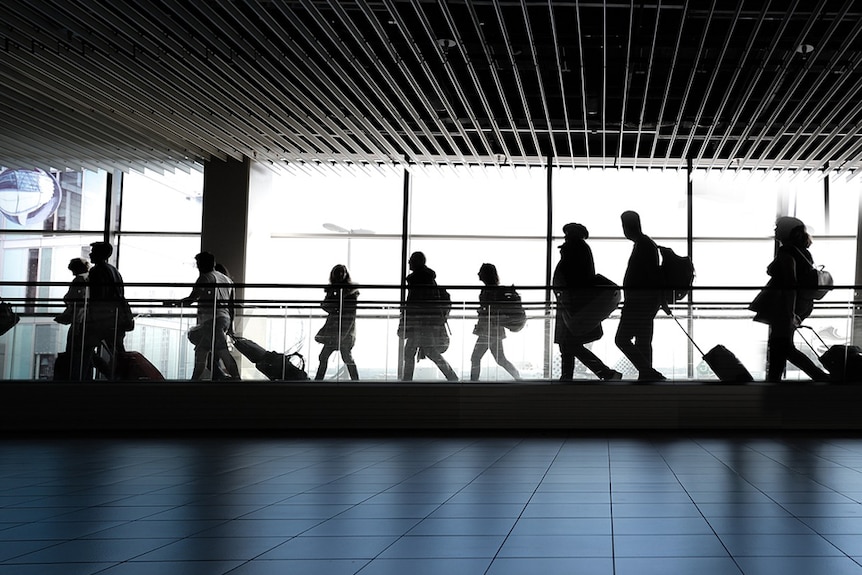 Commuters walking through an unidentified airport, seen in silhouette.