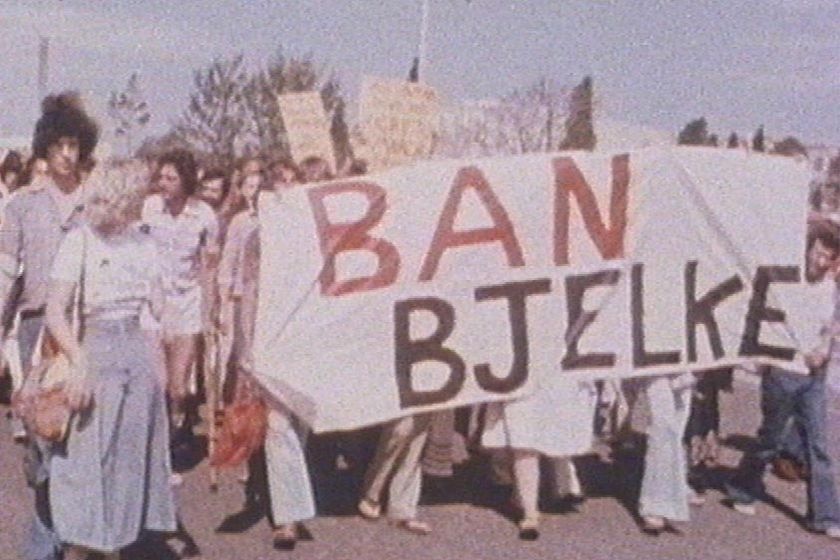 TV still of file image of activists with 'Ban Bjelke' banner in street rally in Brisbane in 1978
