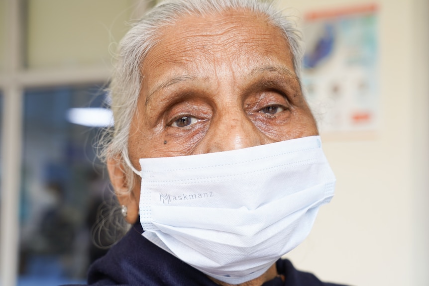 A woman wearing a white mask looks down the barrell of the camera