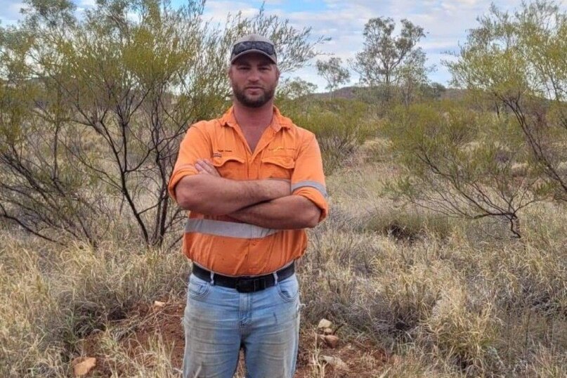 A man stands in a paddock with his arms crossed.