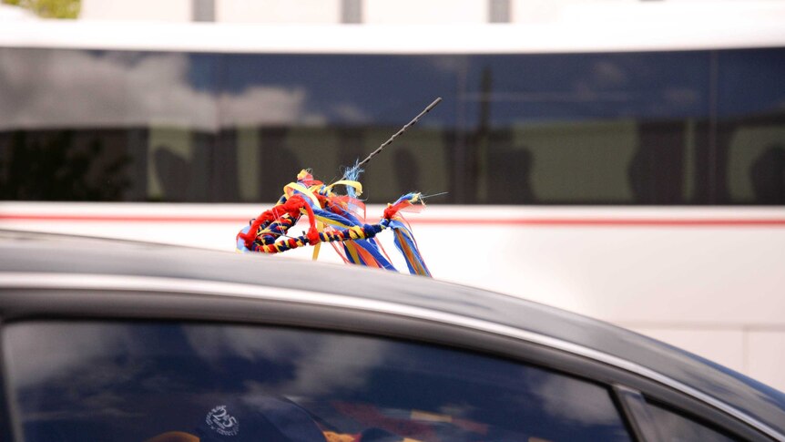 Red, yellow, blue and black ribbons tied to the aerial of a car