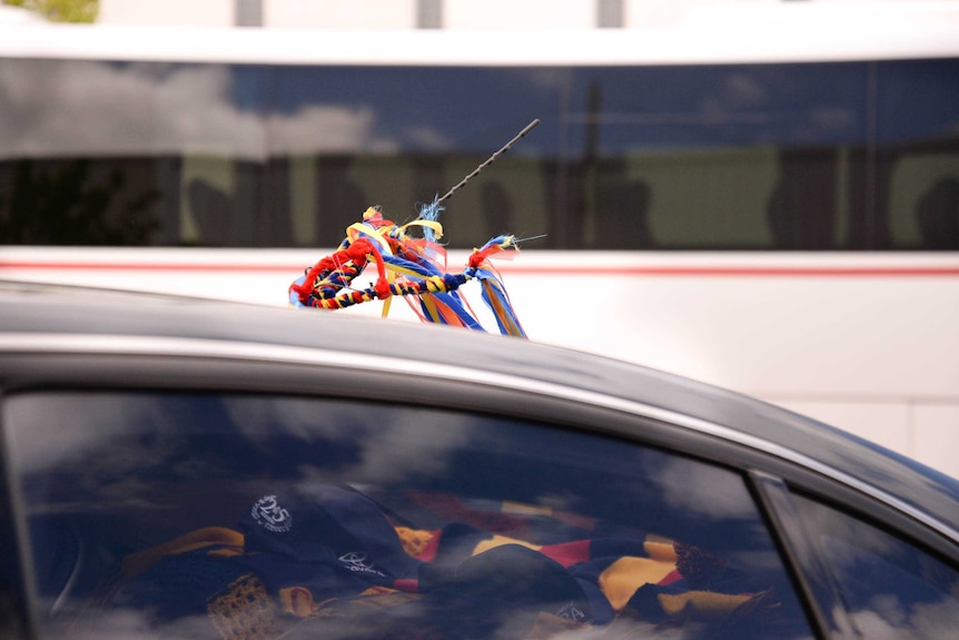 Red, yellow, blue and black ribbons tied to the aerial of a car