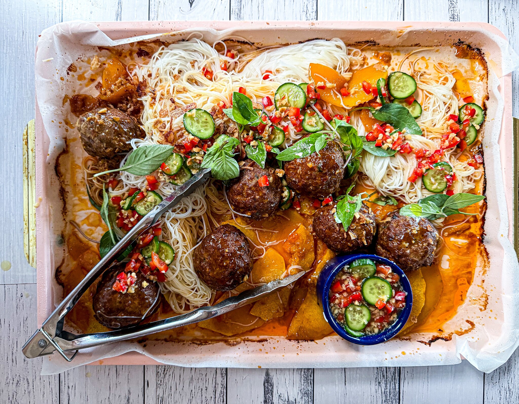A baking tray with Thai-inspired meatballs baked on top of roast pumpkin. Rice vermicelli is added along with quick pickles