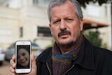 A man looks at the camera as he displays a mobile phone showing a photo of Aiia Maasarwe.