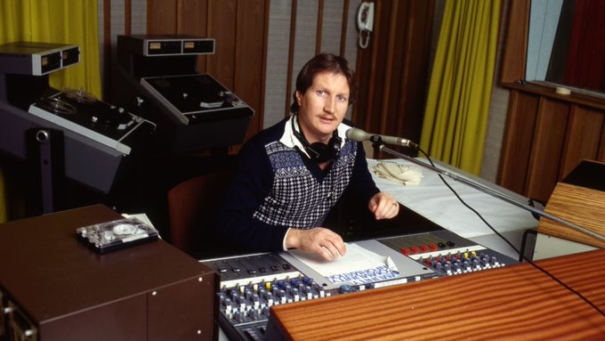 A man sitting in a radio studio behind a microphone