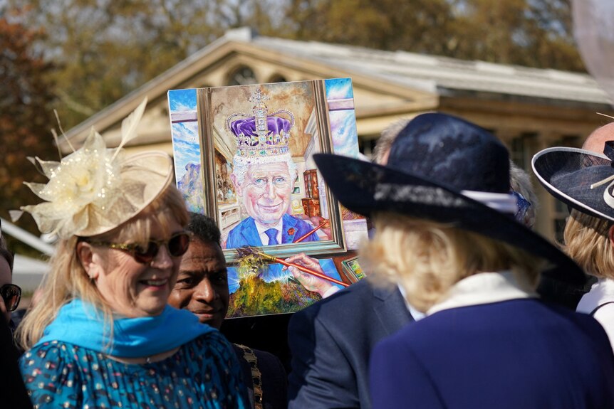 A portrait of King Charles is held up in front of Queen Consort Camilla at the garden party.