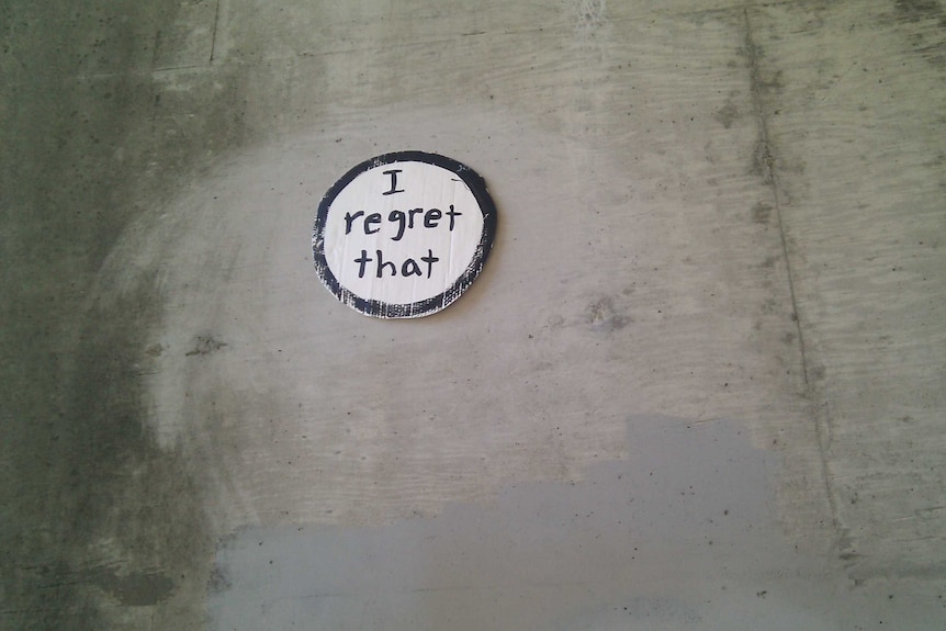 A cardboard circle on a wall that says 'I regret that'