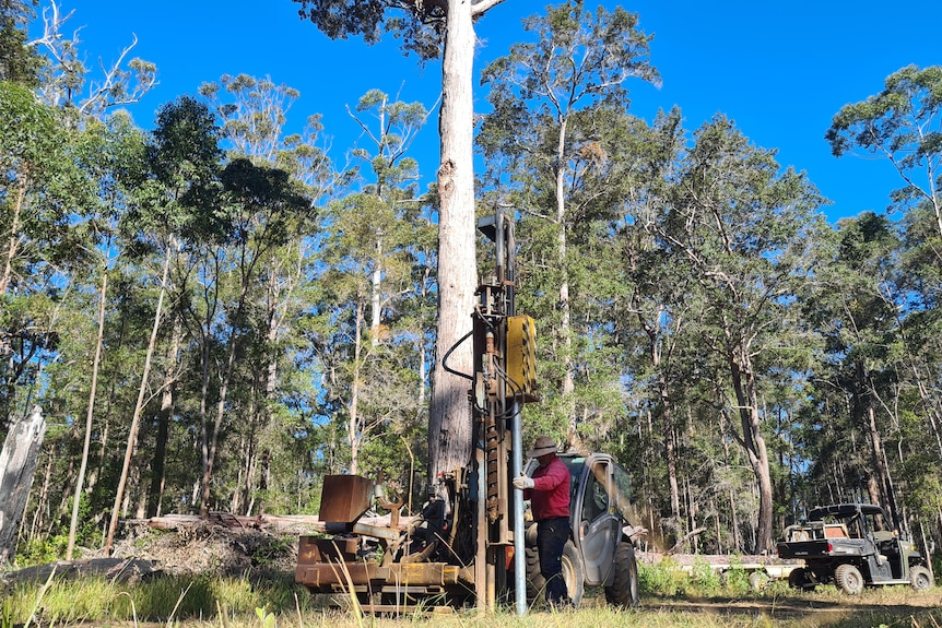 A man stands with machinery as a large fence post is driven into the ground.