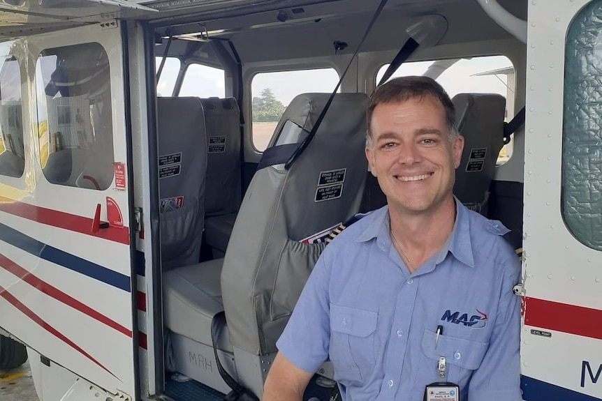 A man sits in the door of a small plane