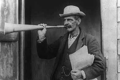 Photo historique en noir et blanc d'un crieur public tenant une trompette, portant un chapeau, une liasse de papiers, une montre de poche en gilet.