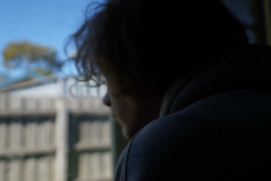 A boy with medium length brown hair is shown side-on, looking out into a backyard.