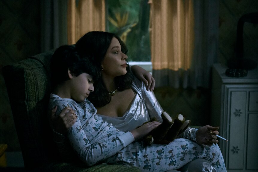A woman sits in a chair at night and cradles a young child.