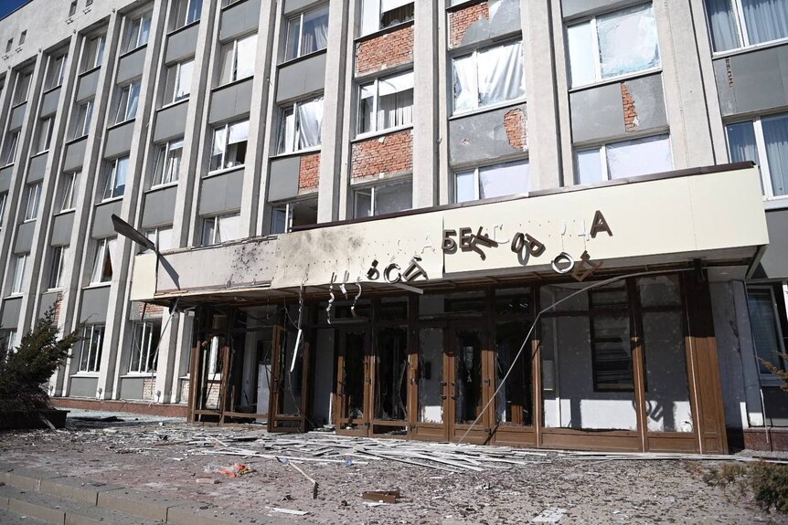 A building stands damaged with shattered glass and broken doors