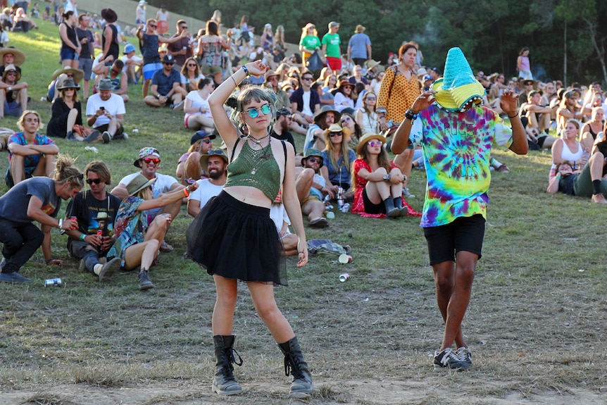 A woman and man in the foreground dancing at Falls Festival with crowd on the hill behind them