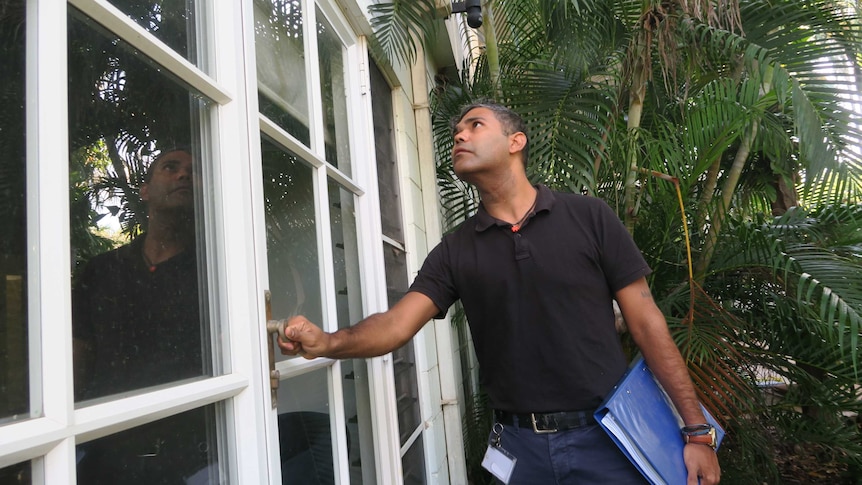 Desmond Campbell stands outside a client's home, with one hand on an external door handle and the other carrying a folder.