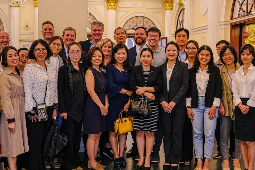 A large group of people smiling together for a group photo. They're standing in an ornately decorated hall 