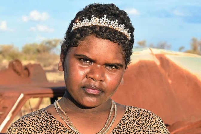 close up photo of young Indigenous girl wearing tiara and leopard print blouse looking at camera