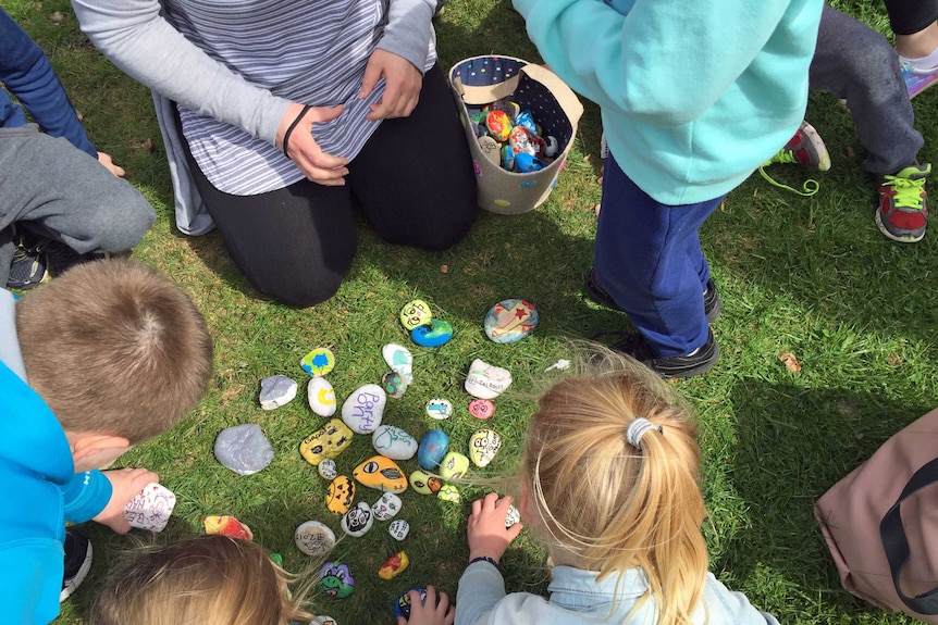 Painted rocks on grass with children looking at them