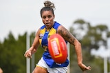 A woman in a West Coast Eagles blue and gold guernsey runs after an AFL football.