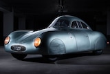 A metallic bubble-like car sits in a dark room.