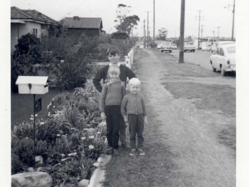 Black and white image of three young children standing in suburban street 