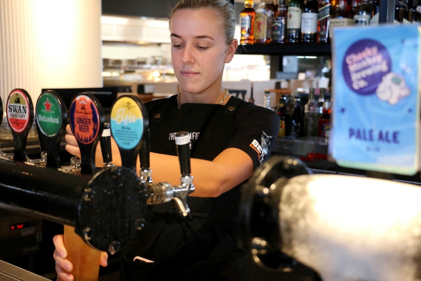 An anonymous staff member pulls out a beer behind the bar.