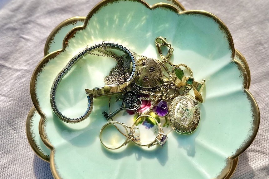 Antique saucer with gold scalloped edge with glistening opal and amethyst rings, locket necklaces and ladies wrist watch