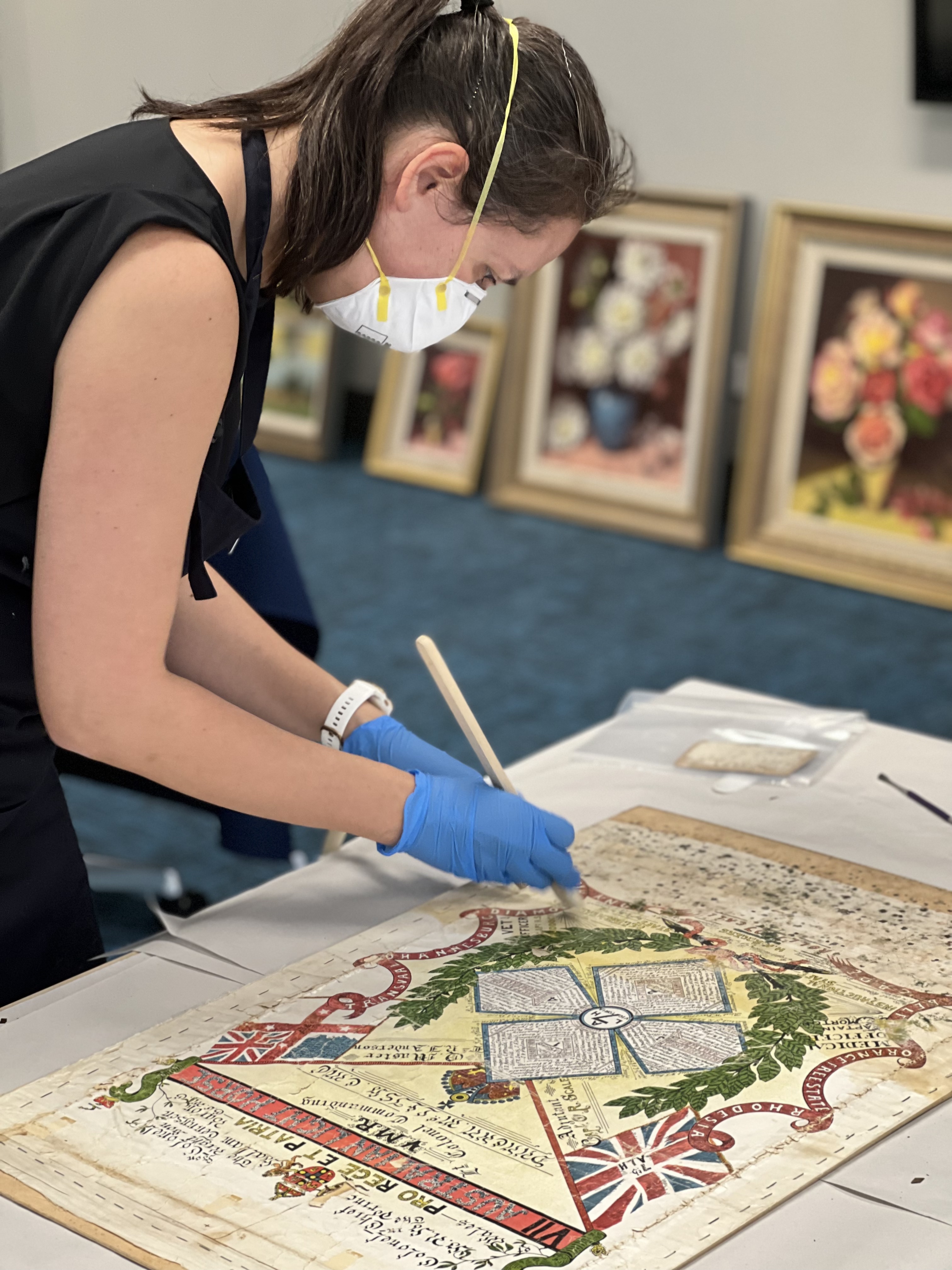 A woman with a mask and gloves brushes a rare print to try and remove mould