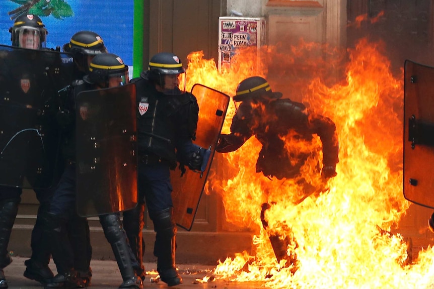 A French riot police officer is surrounded by flames.