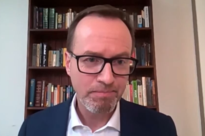 A man with a short, neat beard and haircut, wearing spectacles and a dark suit.