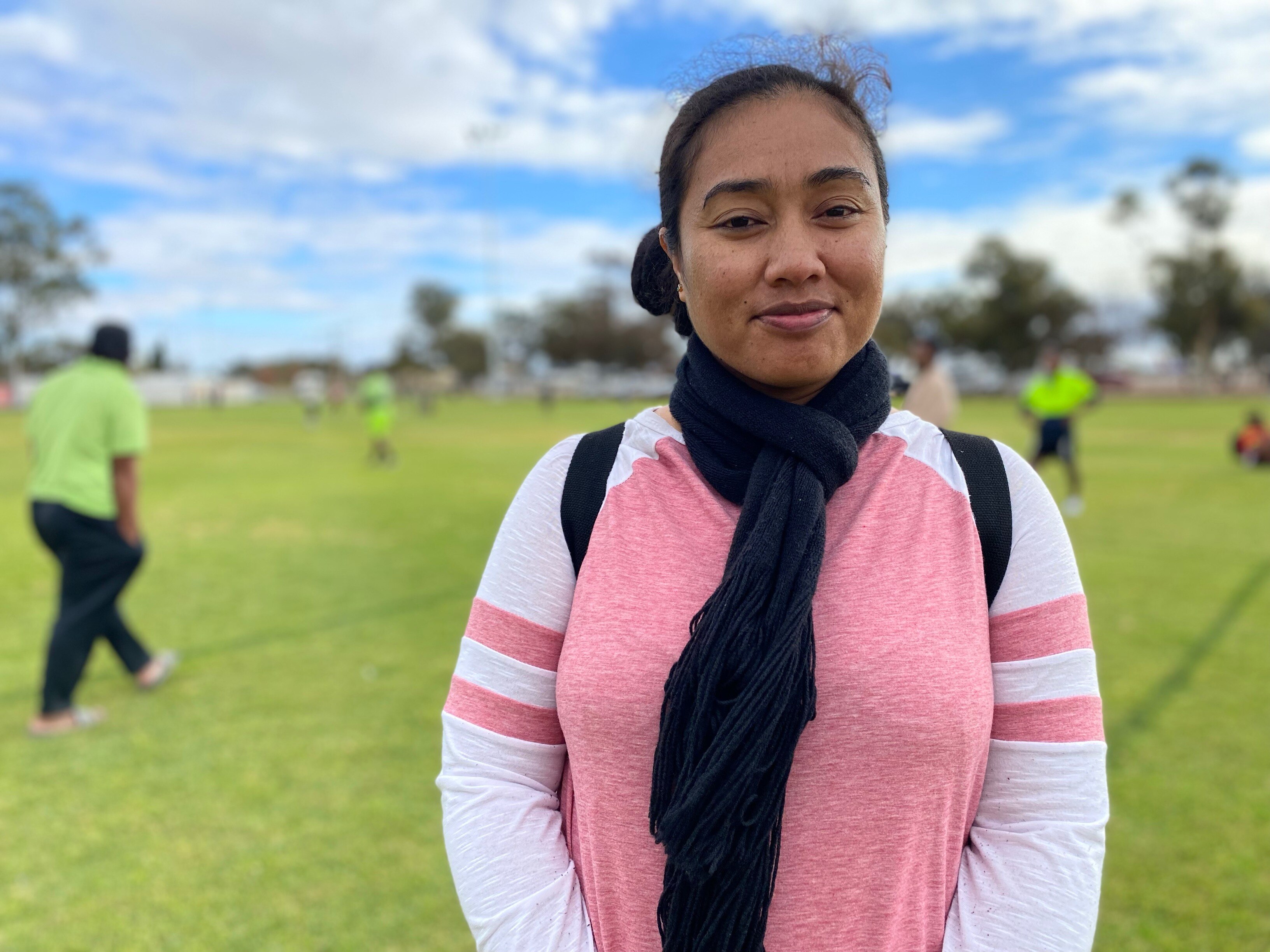 A woman in a pink shirt with white sleeves and a navy blue scarf standing on a soccer pitch
