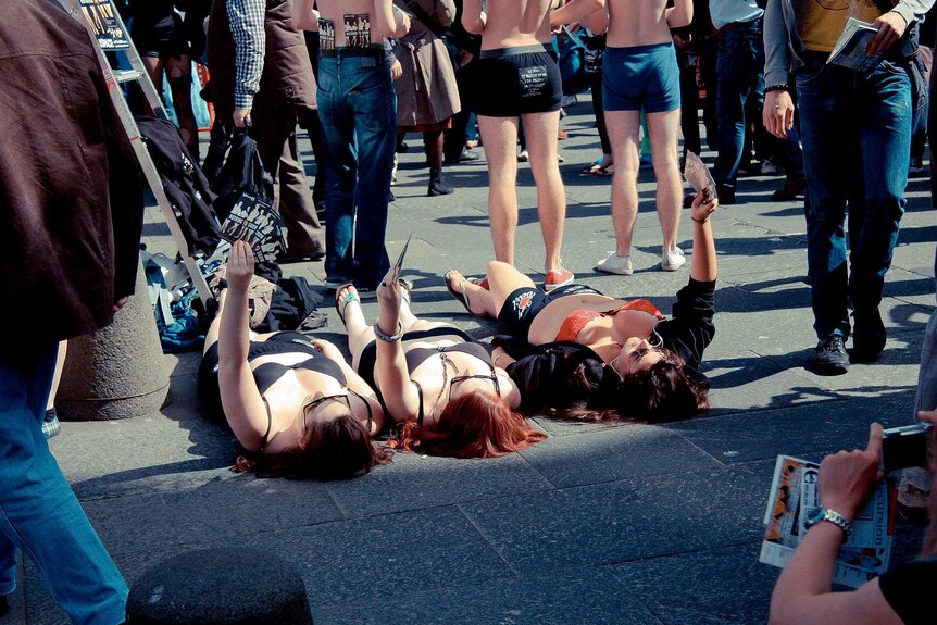 Three women and two men in their underwear hand out fliers to a dense crowd.