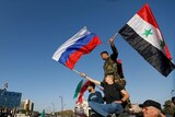 Syrians wave Russian and Syrian flags atop a car during a  protest