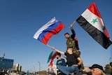 Syrians wave Russian and Syrian flags atop a car during a  protest