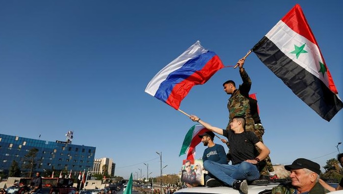 Syrians wave Russian and Syrian flags atop a car during a  protest