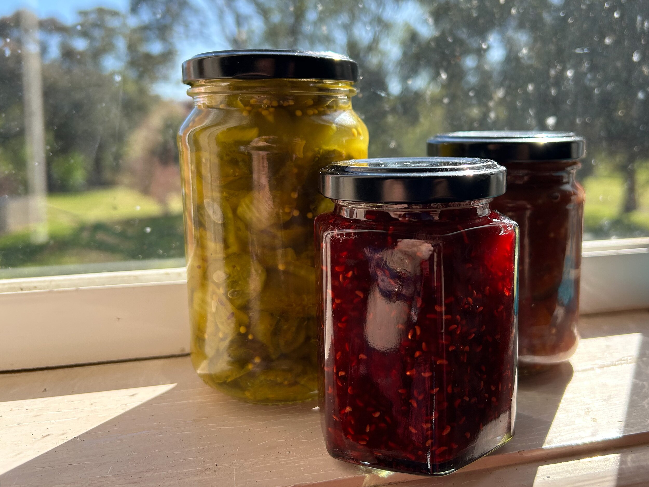 Three jars of colourful homemade preserves sit on a sun-drenched windowsill.